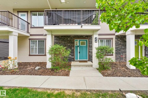 Two-story exterior featuring a vibrant turquoise entrance door, stone facade accents, and horizontal siding - 85 165 Cy Becker Boulevard, Edmonton, AB - Outdoor