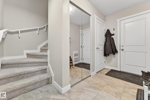 Entryway featuring light-toned tile flooring, a mirrored closet, and a staircase with carpeted treads and white handrails - 85 165 Cy Becker Boulevard, Edmonton, AB - Indoor