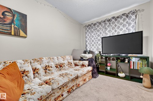Carpeted room featuring light-toned walls, a built-in media console with shelving, and a window with curtains - 85 165 Cy Becker Boulevard, Edmonton, AB - Indoor Photo Showing Bedroom