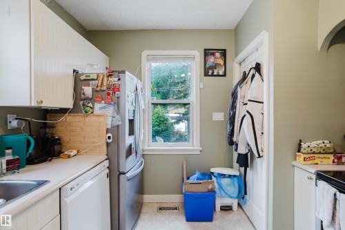 Kitchen featuring white cabinetry, light countertops, a stainless steel refrigerator, and a window providing natural light - 11158 65 Street, Edmonton, AB 