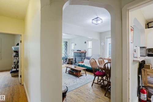 Arched entryway opening to a living area featuring wood-finish flooring, a decorative fireplace with stone surround, and an overhead flush-mount light fixture - 11158 65 Street, Edmonton, AB 