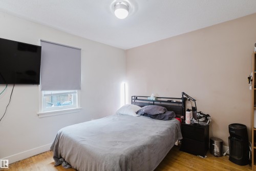 Bedroom with wood-finish flooring, a window featuring a roller shade, and light-toned walls - 11158 65 Street, Edmonton, AB 