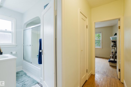 Bathroom featuring a white vanity with an integrated sink, a bathtub with a sliding glass enclosure, and tiled flooring - 11158 65 Street, Edmonton, AB 