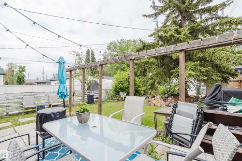 Expansive backyard featuring a wood pergola, string lighting, mature trees, and a combination of paved patio and grassy areas - 11158 65 Street, Edmonton, AB 