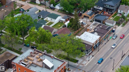 Urban neighborhood featuring a mix of residential and commercial properties, mature trees lining sidewalks, and a prominent commercial building with an outdoor rooftop area - 11158 65 Street, Edmonton, AB 