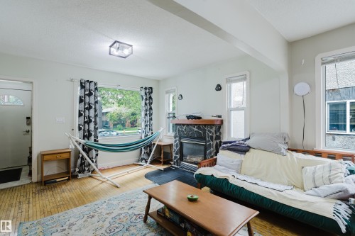 Living area featuring wood-finish flooring, a stone-surround fireplace with a wood mantle, and multiple windows - 11158 65 Street, Edmonton, AB 