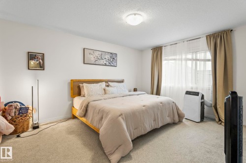Carpeted bedroom featuring neutral wall tones, a large window with drapes, and a ceiling-mounted light fixture - 20227 17Ave, Edmonton, AB 