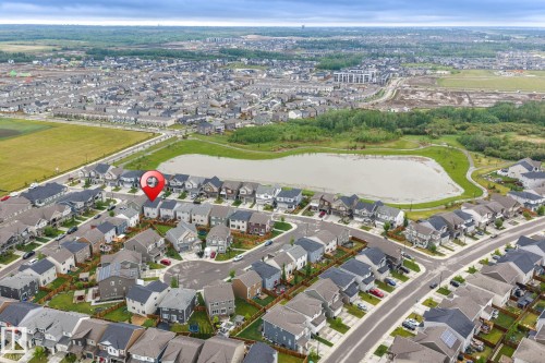 Aerial photograph showcasing a residential neighborhood with a large retention pond, surrounded by green spaces and a walking path - 20227 17Ave, Edmonton, AB 
