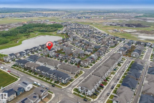 Aerial perspective showcasing a residential development with a prominent pond and green spaces - 20227 17Ave, Edmonton, AB 