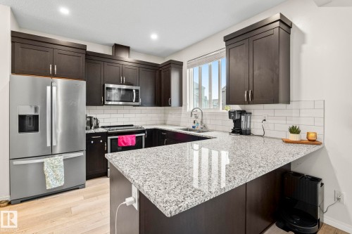 Kitchen featuring dark wood cabinetry, stainless steel appliances, a white subway tile backsplash, and light wood-finish flooring - 20227 17Ave, Edmonton, AB 