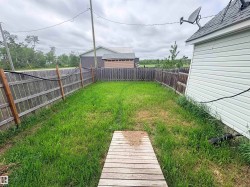 Fenced backyard featuring a wooden walkway, grassed area, and wood panel fencing - 
