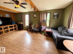 Spacious room featuring wood-finish flooring, exposed ceiling beams, and a ceiling fan with integrated lighting - 