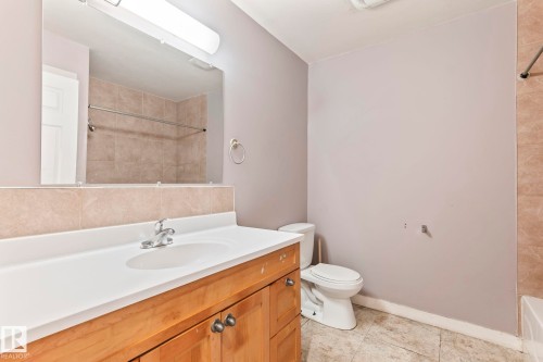 Bathroom vanity with a white countertop and integrated sink, accompanied by a natural wood-finish cabinet - 2045 46St, Edmonton, AB 