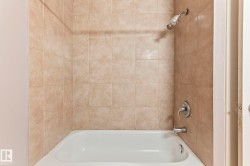 White bathtub with light beige square wall tiling and chrome fixtures - 