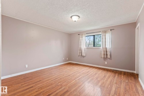 Spacious room featuring wood-finish flooring, a window offering natural light, and a ceiling-mounted light fixture - 2045 46St, Edmonton, AB 