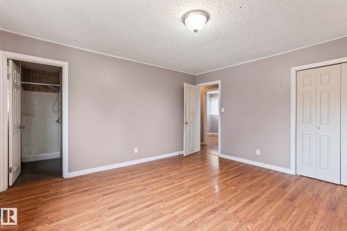Wood-finish flooring throughout, featuring a neutral color palette, ceiling-mounted light fixture, bi-fold closet doors, and an en-suite bathroom with a shower - 2045 46St, Edmonton, AB 