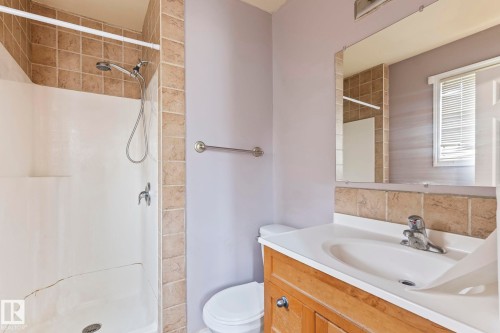 Bathroom with a tiled shower surround, integrated single-handle faucet, and a built-in wood-finish vanity with an integrated sink - 2045 46St, Edmonton, AB 