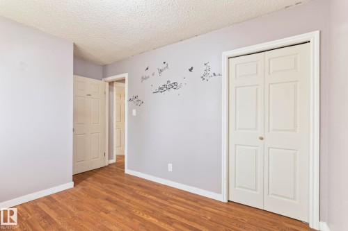 Room featuring wood-finish flooring, light purple walls, and a textured ceiling - 2045 46St, Edmonton, AB 