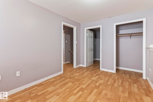Spacious room featuring wood-finish flooring, light gray walls, white trim, and a built-in closet with shelving and hanging rod - 2045 46St, Edmonton, AB 