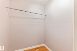 Walk-in closet featuring light-toned walls, wood-finish flooring, white baseboards, and an installed hanging rod - 