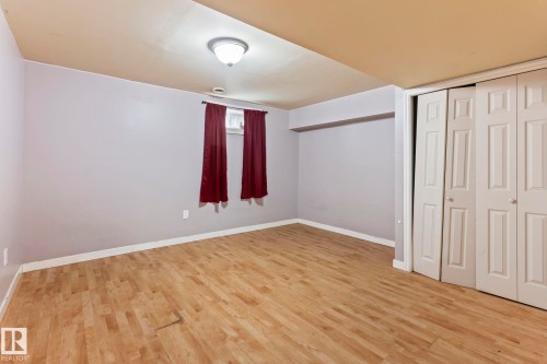Spacious room featuring wood-finish flooring, light grey walls, and a white ceiling - 2045 46St, Edmonton, AB 
