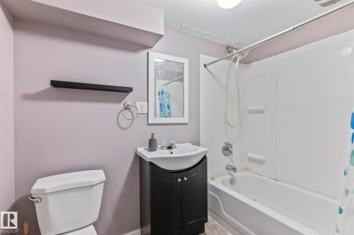 Bathroom featuring a white bathtub, wall-mounted shower, and a dark wood-finish vanity with an integrated sink - 2045 46St, Edmonton, AB 