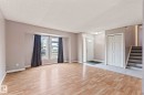 Spacious open-concept room featuring wood-finish flooring, a front entry with tile flooring, an entry door with a decorative glass insert, a built-in closet with bifold doors, and a staircase with wood treads - 2045 46St, Edmonton, AB 