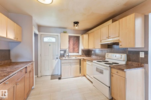 Kitchen featuring light wood-finish cabinetry, laminate countertops, and a dark tile backsplash - 2045 46St, Edmonton, AB 