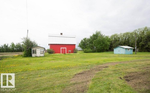 Expansive green space featuring a large red barn with a white metal roof, a smaller light blue outbuilding with a white window, and a third weathered utility structure - 2021 Twp Rd 604, Rural Westlock County, AB 
