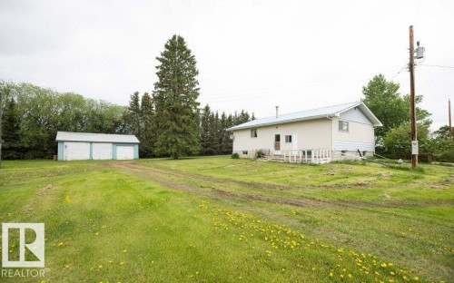 Spacious lot featuring a detached three-car garage with light blue siding and white doors, a light-colored exterior residence with a light blue metal roof, and surrounding mature trees - 2021 Twp Rd 604, Rural Westlock County, AB 