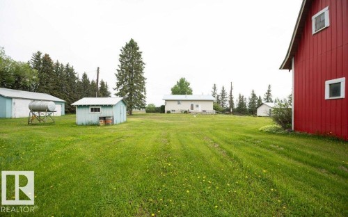Expansive green space featuring multiple outbuildings, including a prominent red barn structure with white-framed windows, a light blue utility shed with a window, and a white garage-style building with a metal roof - 2021 Twp Rd 604, Rural Westlock County, AB 