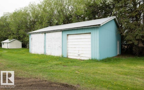 Two outbuildings on a grassy lot, featuring a larger structure with light blue siding and a white garage door, alongside a smaller white shed - 2021 Twp Rd 604, Rural Westlock County, AB 