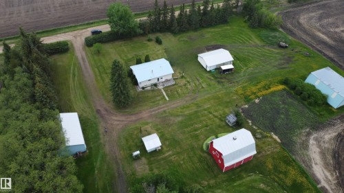Spacious rural property featuring a primary residence with a light-colored roof, multiple outbuildings including a red barn, a white utility building, and a light-blue storage structure - 2021 Twp Rd 604, Rural Westlock County, AB 