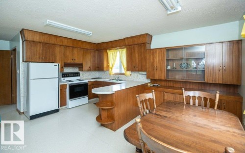 Kitchen featuring wood-finish cabinetry, white appliances, and a built-in breakfast bar - 2021 Twp Rd 604, Rural Westlock County, AB 