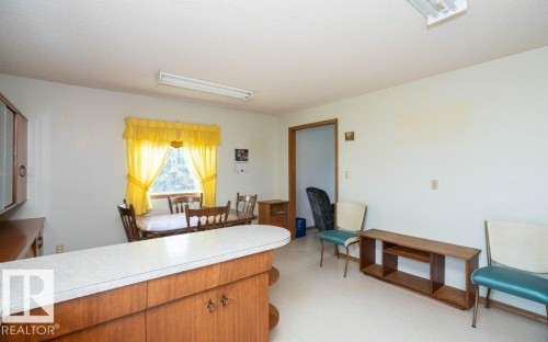Spacious room featuring a breakfast bar with wood-finish cabinetry and a light-toned countertop, a window with natural light, and a fluorescent ceiling light fixture - 2021 Twp Rd 604, Rural Westlock County, AB 