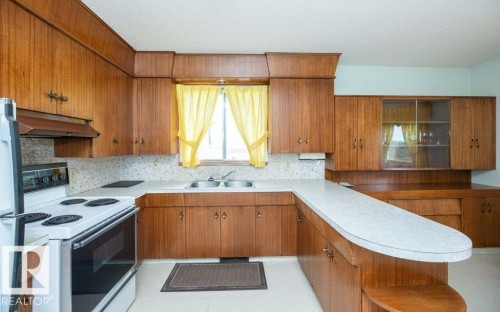 U-shaped kitchen featuring wood-finish cabinetry, a built-in oven, and an integrated double basin sink - 2021 Twp Rd 604, Rural Westlock County, AB 