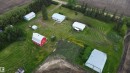 Aerial view of an agricultural property featuring multiple outbuildings, including a classic red barn with a gambrel roof and two large metal-sided structures - 2021 Twp Rd 604, Rural Westlock County, AB 