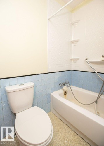 Bathroom featuring a white toilet, blue tiled wainscoting, and a white bathtub with a textured surround - 2021 Twp Rd 604, Rural Westlock County, AB 