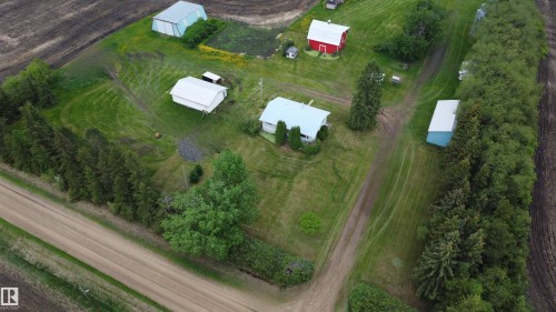Aerial view showcasing a residential property with multiple outbuildings, bordered by agricultural fields and a dirt road - 2021 Twp Rd 604, Rural Westlock County, AB 