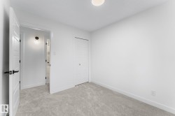 Neutral-toned carpeting and white walls define this room, featuring a white door with black hardware, a flush-mount ceiling light, and a built-in closet with white bifold doors - 