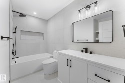 Bathroom featuring a white vanity with black hardware, a rectangular mirror, and an overhead three-light fixture - 