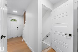 Bright entry foyer featuring wood-finish flooring, a white paneled front door with an arched glass insert, and a circular recessed light - 