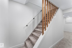 Carpeted staircase featuring a light wood-finish spindle railing and a white handrail - 
