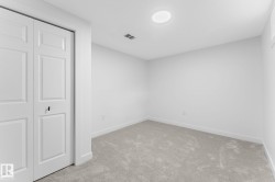 Interior room featuring neutral-toned carpeting, white walls, and white bi-fold closet doors with black hardware - 