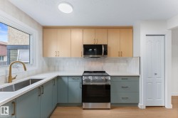 Modern kitchen featuring light wood-finish upper cabinetry and matte blue-green lower cabinetry with brushed brass hardware - 