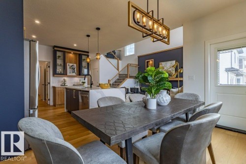 Open-concept living space featuring wood-finish flooring, a contemporary kitchen with stainless steel appliances, and a dining area with a modern chandelier - 82 Wynn Rd, Fort Saskatchewan, AB 