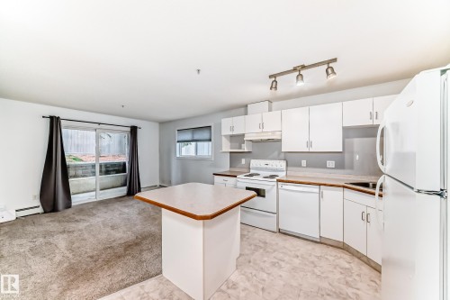 Open-concept kitchen featuring white cabinetry, track lighting, an island with a light wood-finish countertop, and white appliances - 126 10535 122 Street, Edmonton, AB 