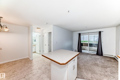 Open-concept living area featuring a kitchen island with storage, sliding glass doors to private patio. - 126 10535 122 Street, Edmonton, AB 