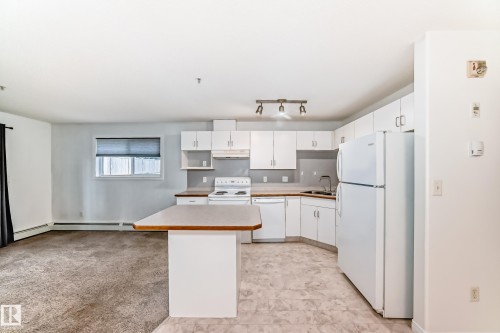 Open-concept kitchen featuring white cabinetry, light-toned countertops, and a full suite of white appliances - 126 10535 122 Street, Edmonton, AB 
