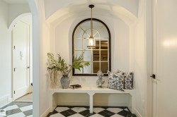 Arched entryway featuring a black and white checkerboard tile floor, an integrated white bench, and a gold-finished pendant light - 